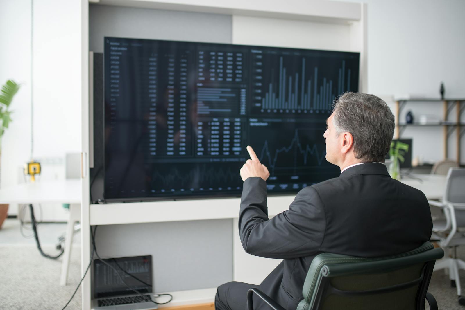 A businessman sitting and analyzing financial data on a large screen in an office.